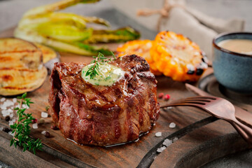 Large grilled Filet Mignon steak with butter and thyme served on a wooden board. Grilled meat dish with vegetables
