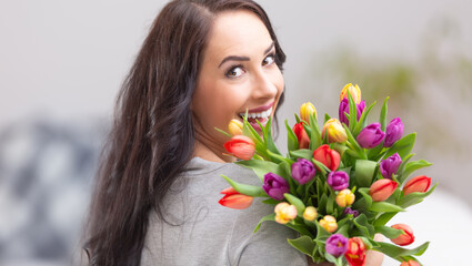 Happy dark haired woman holding a lovely bouquet full of tulips during national womens day