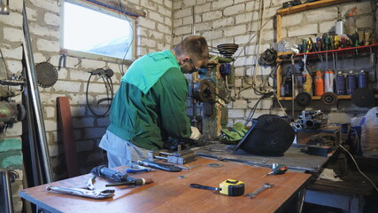 Male mechanic in protective glasses working on manufacturing machine at workshop. Young repairman in uniform fixing metal details in garage. Concept of maintenance service. Close up Slow motion