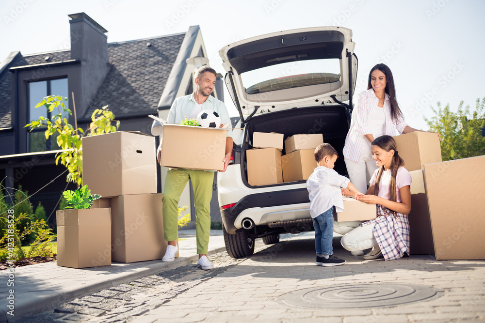 Poster Portrait of attractive cheerful family moving to new place carrying bringing belongings cardboard in cottage town outdoor