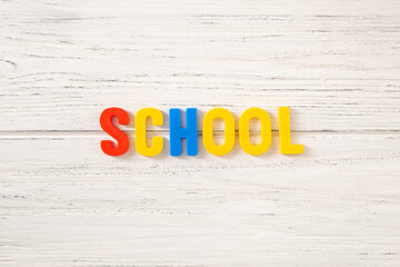 The sign, word school on a white wooden background, top view. Kids colored plastic letters