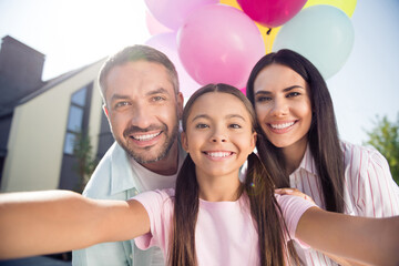 Self-portrait of attractive cheerful family mommy daddy holding air balls having celebrating day in cottage town outdoor