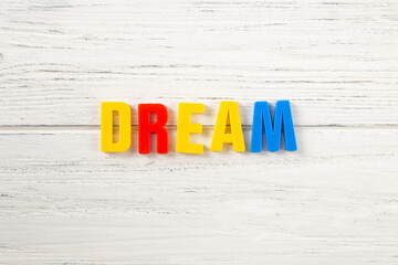 The sign, word dream on a white wooden background, top view. Children colored plastic letters