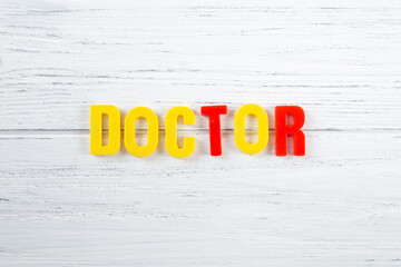 The sign, word doctor on a white wooden background, top view. Children colored plastic letters, kids health