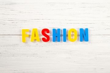 The sign, word fashion on a white wooden background, top view. Kids colored plastic letters