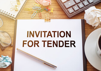 On a wooden table there is an office sheet of paper with the text INVITATION FOR TENDER. Business workspace with calculator, glasses, pen, crumpled paper and cup of coffee.