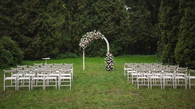 Beautiful romantic place outdoors made with white wooden rounded frame and fresh floral roses decorations for outside wedding ceremony in garden. Wedding settings in scenic place