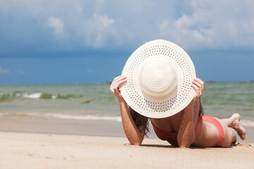 Beautiful woman in bikini and straw hat sunbathing at the seaside
