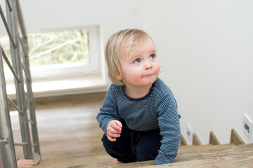 Naklejka premium Small caucasian baby crawling on the stairs. Indoor portrait with copy space. Kid danger and safeness at home.