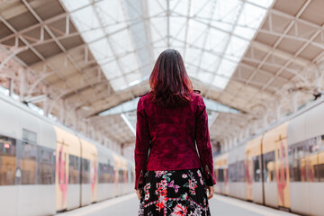 back view of caucasian woman in train station waiting to travel. Travel and lifestyle concept