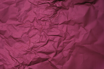 Dark red background from wrapping crumpled paper. Burgundy sheet of crumpled paper top view. The creases on the surface close-up.