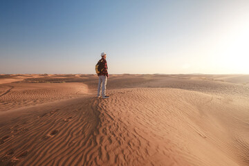 Fototapeta na wymiar Desert adventure. Young man with backpack walking on sand dune. Dubai, United Arab Emirates