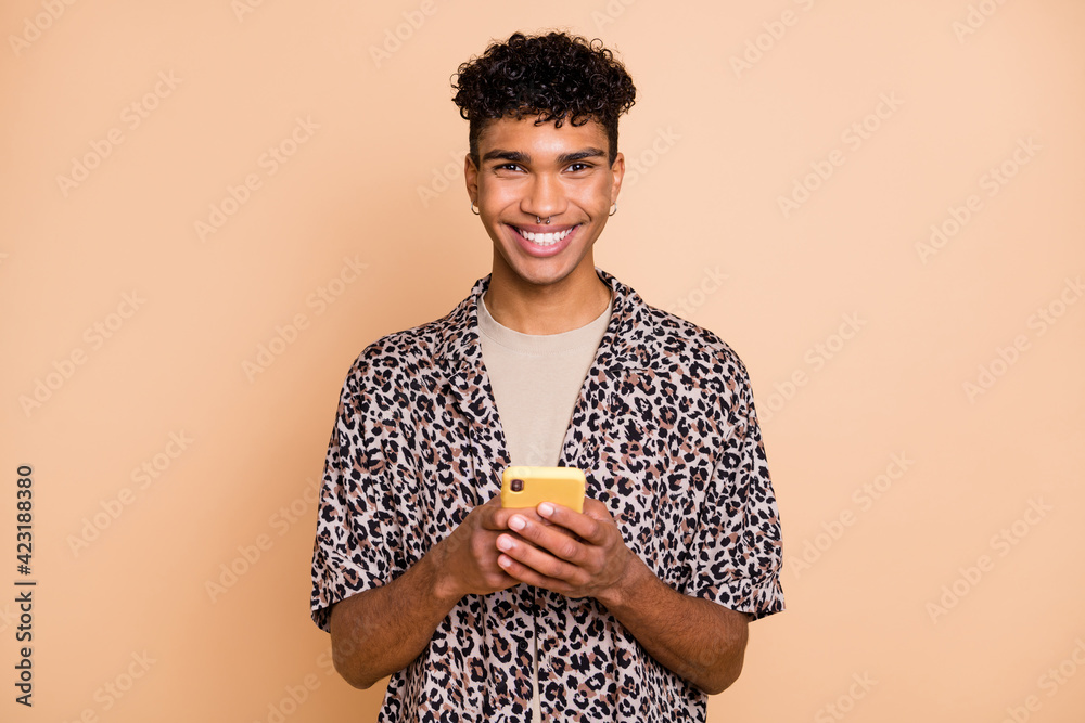 Poster Portrait of brunet optimistic guy hold telephone wear modern shirt isolated on pastel beige color background