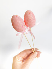 fingers holding two sticks with decorative easter eggs on white background