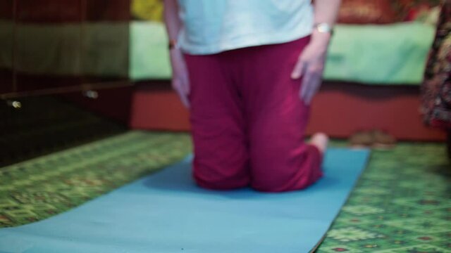 Seniour woman does tibetian gymnastics as morning exercises. Isolation of old people at home during pandemic.