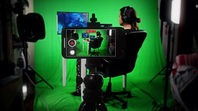 Live Stream Boy Gamer Smartphone On Green Screen Online Games. Long haired male teenager gaming online and streaming while filming with a smartphone on a green screen background