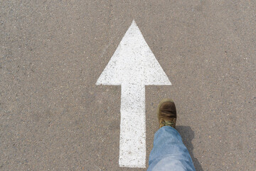White arrow on the asphalt. A man's foot in a boot steps forward. The concept of showing the way,...