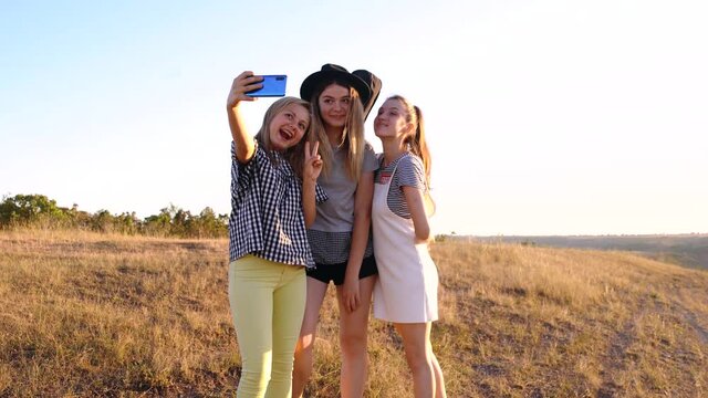 Three pretty young women of 20 years, European, take pictures with the phone during a trip. Young people dressed in color.