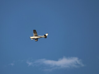 Aeronave de ala alta, volando sobre un cielo azul, con algunas nubes blancas.