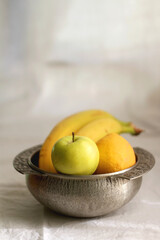 Naklejka na ściany i meble Antique bowl with bananas, apples and lemons. Selective focus, white textile background.