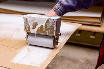Carpenter smears the plywood with hand roller tool, spreader for evenly application of glue on the...