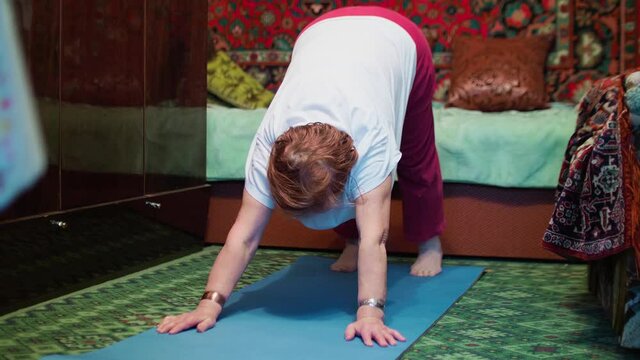 Seniour woman does tibetian gymnastics as morning exercises. Isolation of old people at home during pandemic.