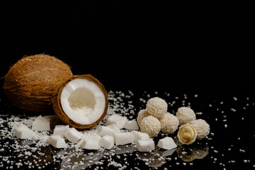 one whole coconut and half a coconut. Coconut slices with coconut shavings on a black background.