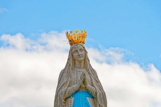 detail of the statue of the virgin Mary in Lourdes in front of a cloudy and blue sky: "our lady of Lourdes"