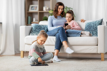 Fototapeta na wymiar people, family and technology concept - happy mother and two daughters with smartphone at home