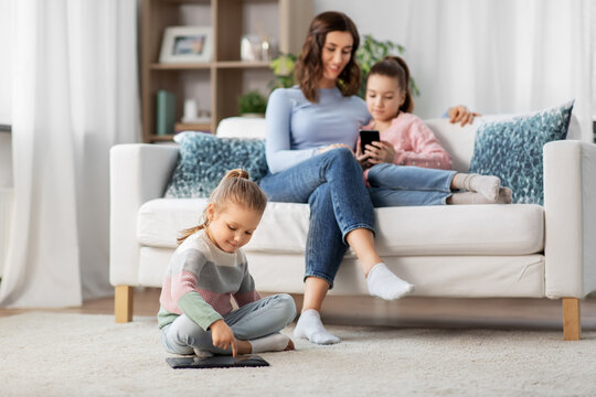 people, family and technology concept - happy mother and two daughters with smartphone at home