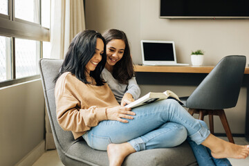 Single parenthood. Mother and daughter reading a book together at home.