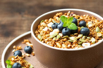 Homemade organic buckwheat granola with blueberries, hazelnuts, peanuts, nutmeg, pumpkin seeds and flax in a ceramic bowl on a brown background. Healthy vegetarian breakfast closeup