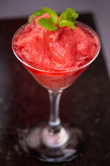 Frozen Strawberry daiquiri cocktail in front of dark background garnished with mint leaves