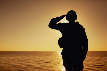 Silhouette of soldier in combat helmet and ammunition saluting on background of sunset sky. Army...