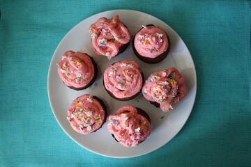 A small shaped cupcake with pink cream and sprinkles on a white plate.