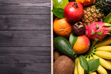 Crate with different exotic fruits on black wooden table, top view. Space for text