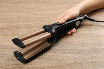 Woman holding modern triple curling iron on wooden background, closeup