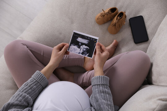Young pregnant woman with ultrasound picture of baby on sofa, above view
