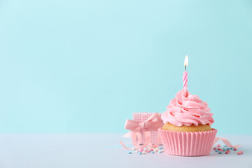 Delicious birthday cupcake with burning candle, sprinkles and gift box on white table against...