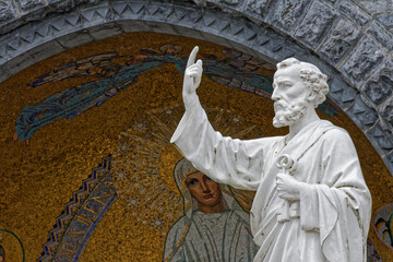 Statue of Saint Peter in Lourdes, in front of the basilica. close up view of the bust in front of a decorated alcove in the sacred square