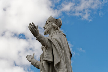 Statue of a saint at the Basilica of Lourdes in France, a sacred place of pilgrimage. Statue of Saint Martin raising his arms to the sky in front of a cloudy and blue sky