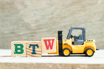Fotobehang Toy forklift hold letter block W to complete word BTW (Abbreviation of by the way) on wood background © bankrx