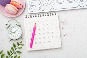 Calendar with pink pencil, macarons and clock on marble background