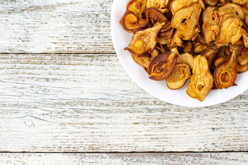 A pile of dried pears in slices on a white plate on wooden background. Dried fruit chips. Healthy food