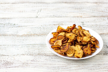 A pile of dried pears in slices on a white plate on wooden background. Dried fruit chips. Healthy food