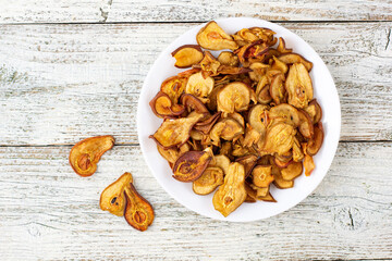 A pile of dried pears in slices on a white plate on wooden background. Dried fruit chips. Healthy food