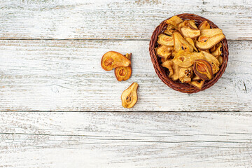 A pile of dried slices of pears in wicker basket on white wooden background. Dried fruit chips. Healthy food