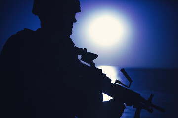 Silhouette of army infantryman standing with light machine gun on background of night sky with...