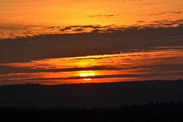 The sun is behind the clouds during an enchanting sunset over a forest near Schweinfurt
