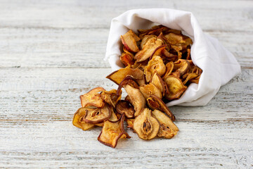 A pile of dried slices of pears pills out of a white pouch on wooden background. Dried fruit chips. Healthy food